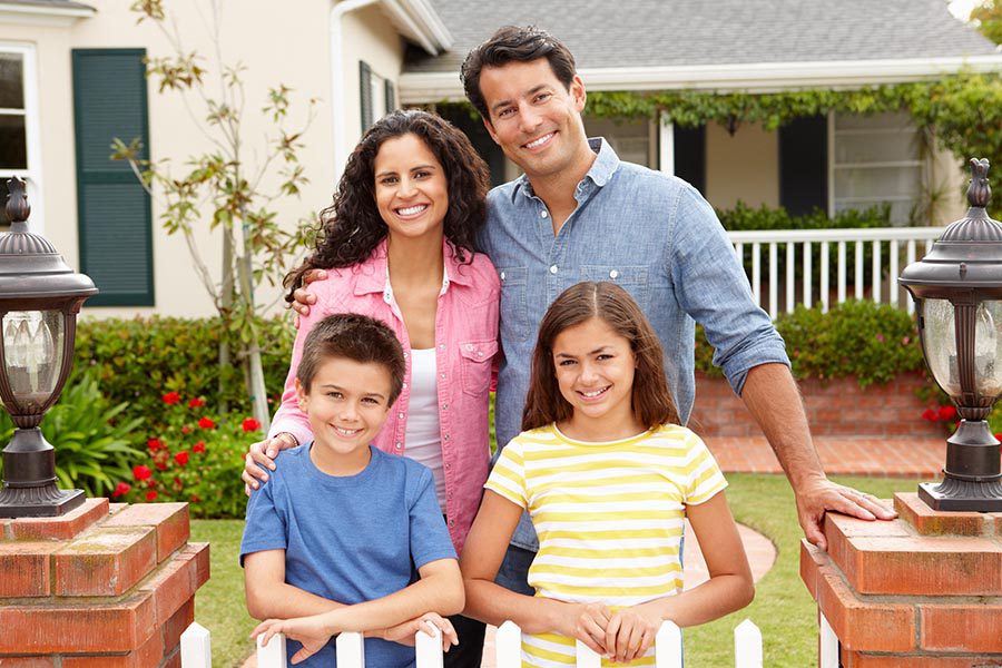 Personal Insurance - Family Stands at Their White Picket Fence in Front of a Beautiful Home, Two Kids in Front of Their Parents